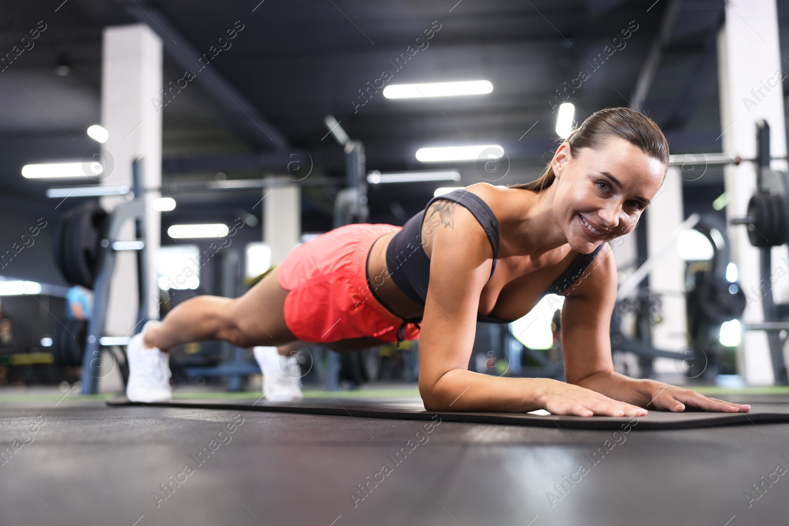 Smiling woman doing plank exercise on yoga mat in gym Photo of Smiling woman doing plank exercise on yoga mat in gym