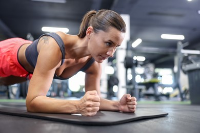 Photo of Athletic woman doing plank exercise on yoga mat in gym