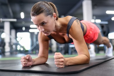 Photo of Athletic woman doing plank exercise on yoga mat in gym