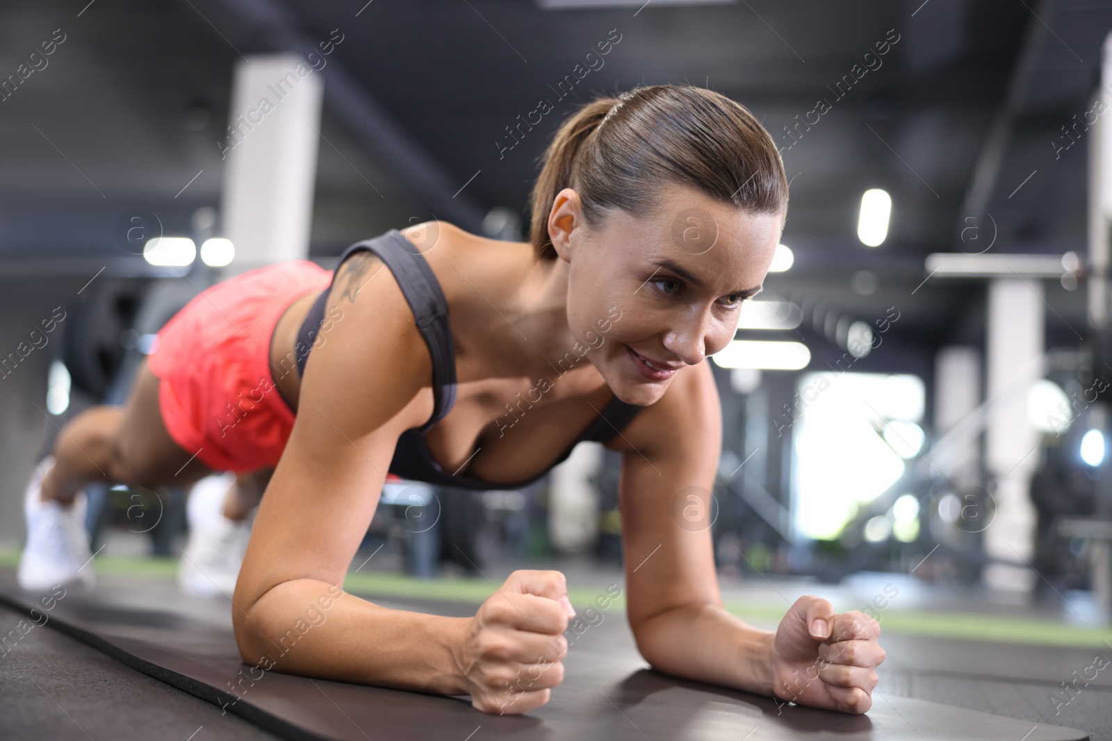 Smiling woman doing plank exercise on yoga mat in gym Photo of Smiling woman doing plank exercise on yoga mat in gym