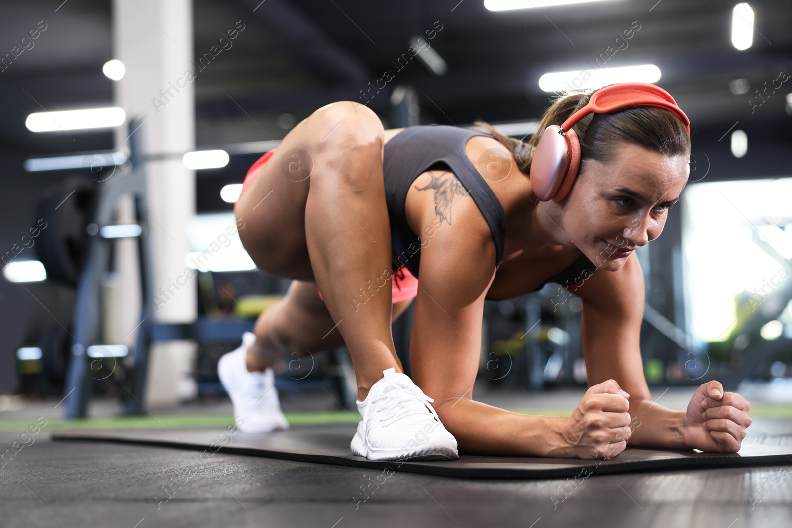 Athletic woman in headphones doing exercise on yoga mat in gym Photo of Athletic woman in headphones doing exercise on yoga mat in gym