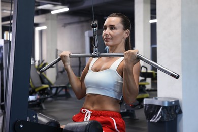 Photo of Athletic woman training on lat pulldown machine in gym