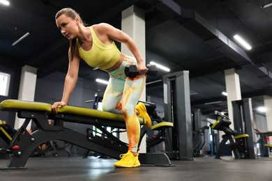Photo of Athletic woman training with dumbbell on exercise bench in gym, low angle view. Space for text