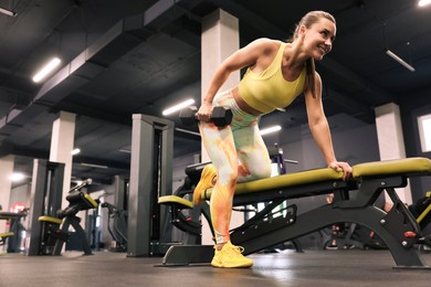 Photo of Smiling woman training with dumbbell on exercise bench in gym, low angle view. Space for text