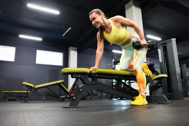 Photo of Smiling woman training with dumbbell on exercise bench in gym, low angle view. Space for text