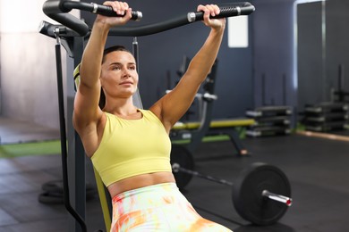 Photo of Athletic woman training on shoulder press machine in gym