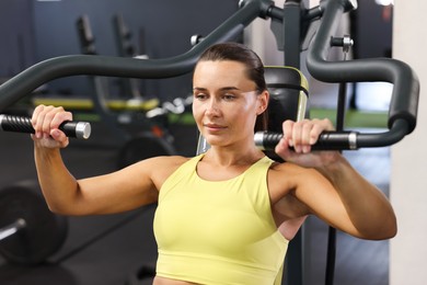 Photo of Athletic woman training on shoulder press machine in gym