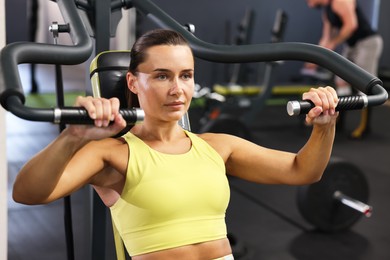 Photo of Athletic woman training on shoulder press machine in gym
