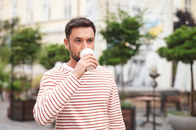 Photo of Coffee to go. Man with paper cup of drink on city street, space for text