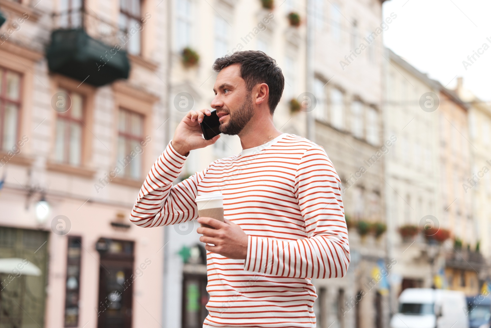 Photo of Coffee to go. Man with paper cup of drink talking on smartphone outdoors