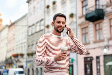 Photo of Coffee to go. Man with paper cup of drink talking on smartphone outdoors