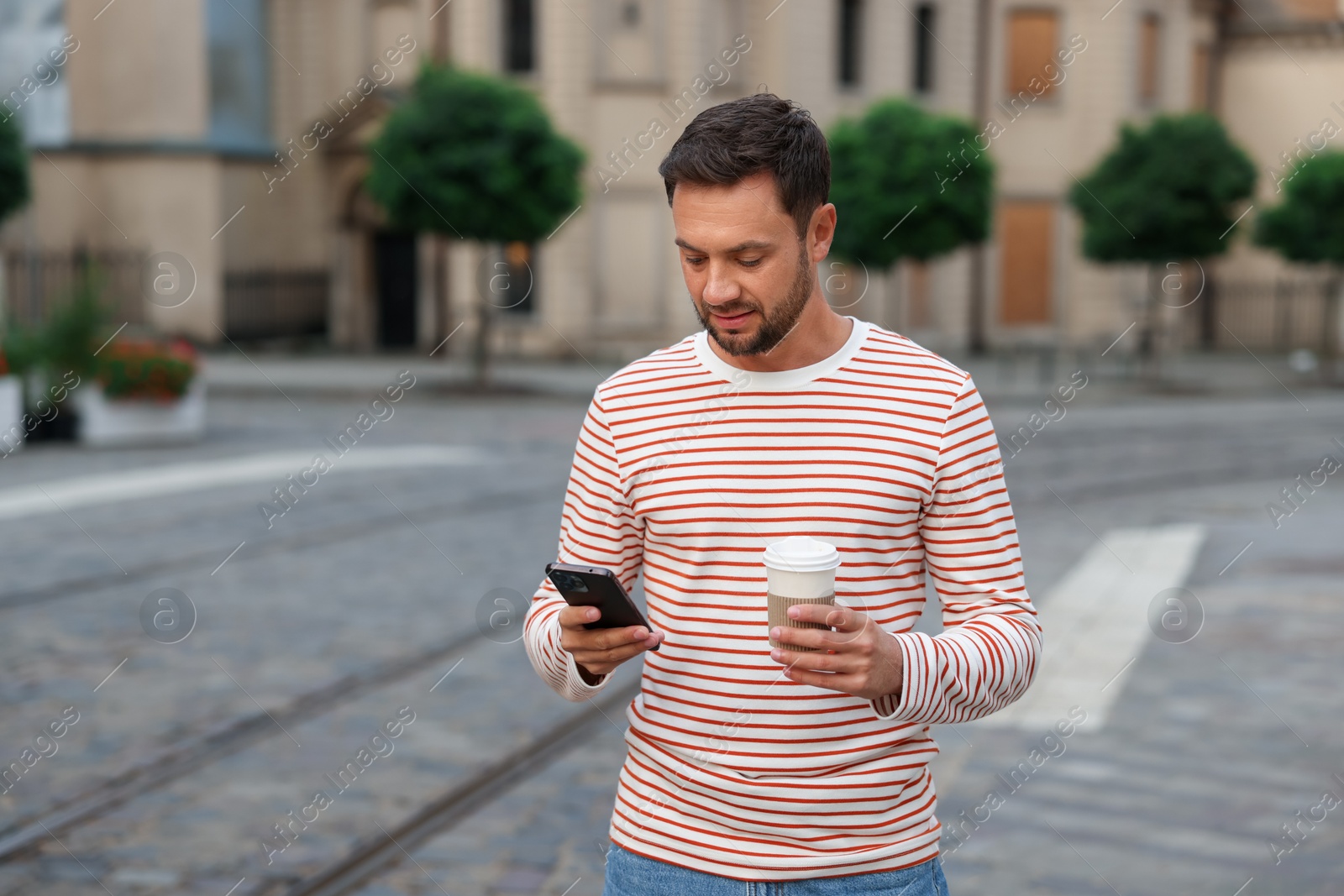 Photo of Coffee to go. Man with paper cup of drink and smartphone on city street, space for text