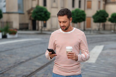 Photo of Coffee to go. Man with paper cup of drink and smartphone on city street, space for text