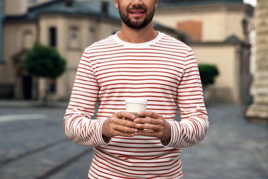 Photo of Coffee to go. Man with paper cup of drink on city street, closeup