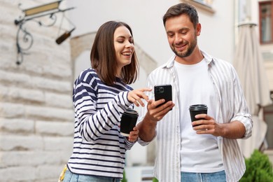 Photo of Coffee to go. Couple with paper cups of drinks and smartphone on city street