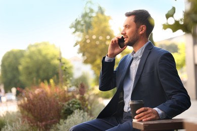 Photo of Coffee to go. Man with paper cup of drink talking on smartphone outdoors, space for text