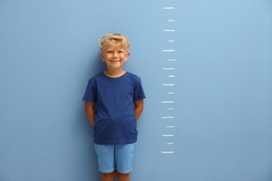 Photo of Cute little boy measuring his height near blue wall