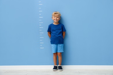 Photo of Cute little boy measuring his height near blue wall