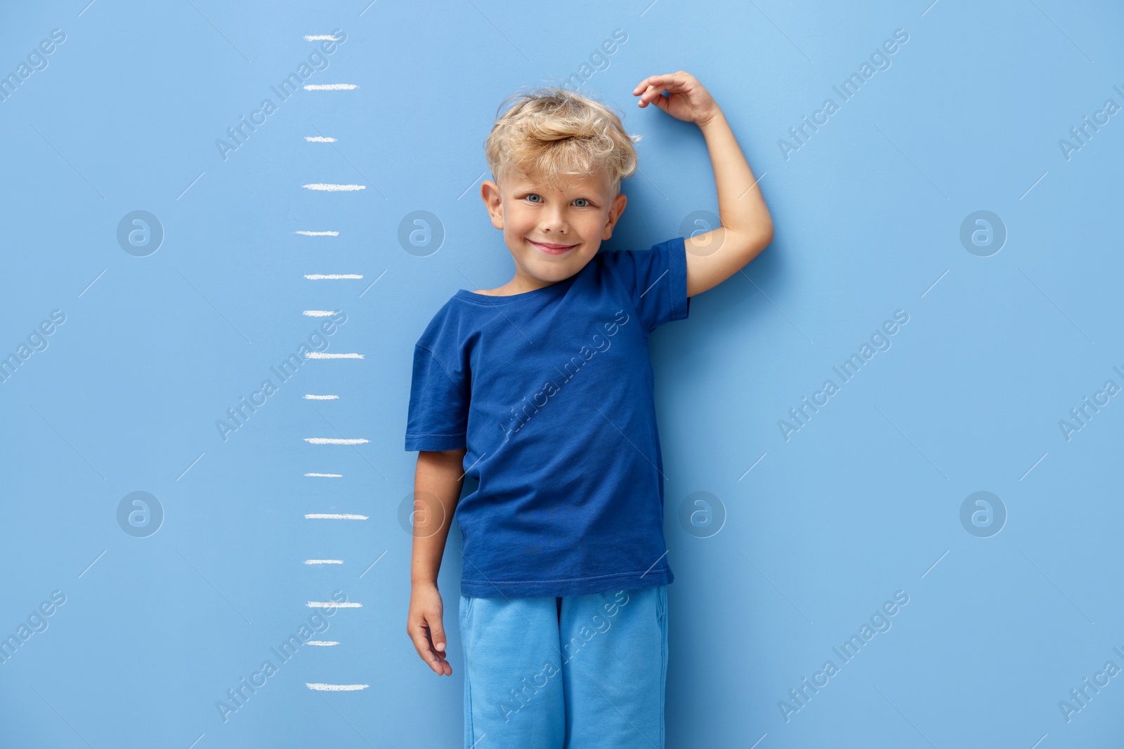 Photo of Cute little boy measuring his height near blue wall