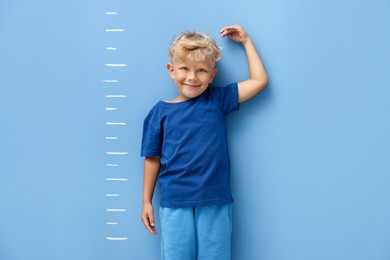 Photo of Cute little boy measuring his height near blue wall
