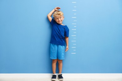Photo of Cute little boy measuring his height near blue wall