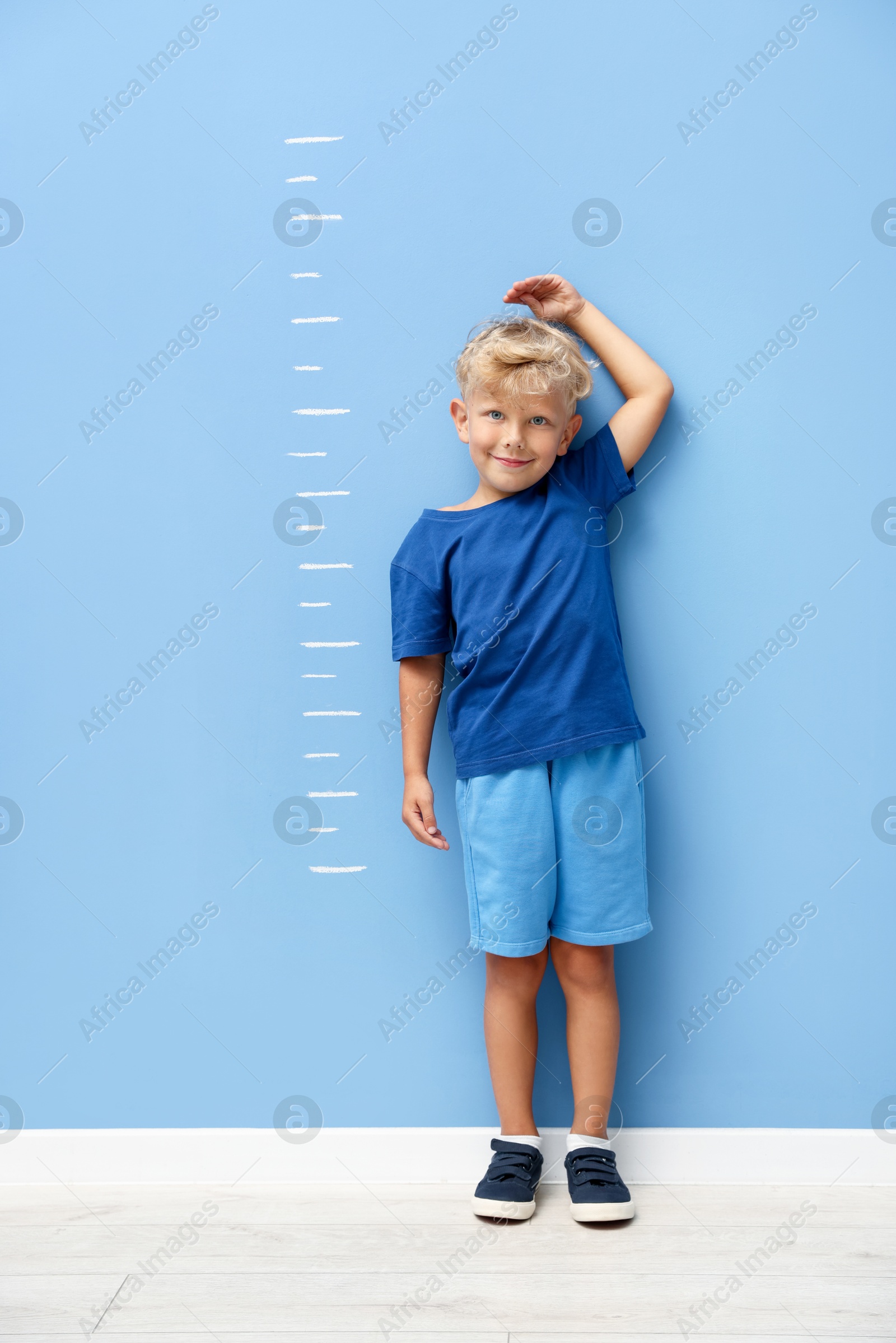Photo of Cute little boy measuring his height near blue wall