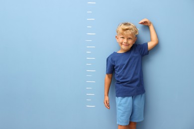 Photo of Cute little boy measuring his height near blue wall. Space for text