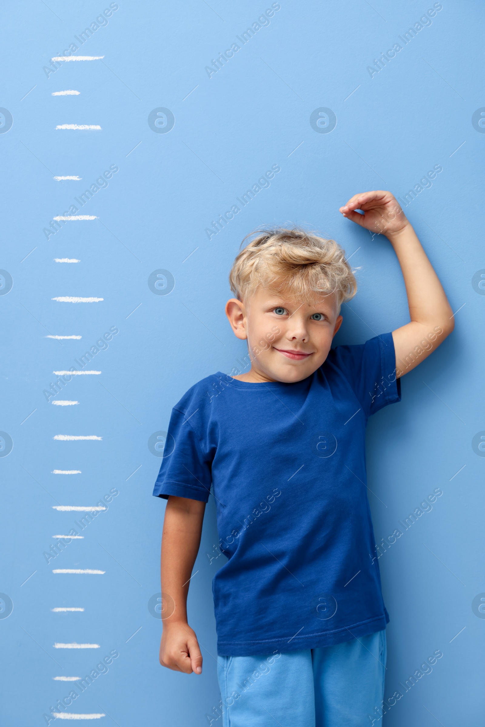 Photo of Cute little boy measuring his height near blue wall