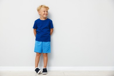 Photo of Cute little boy standing near light wall. Space for text