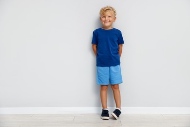 Photo of Cute little boy standing near light wall. Space for text