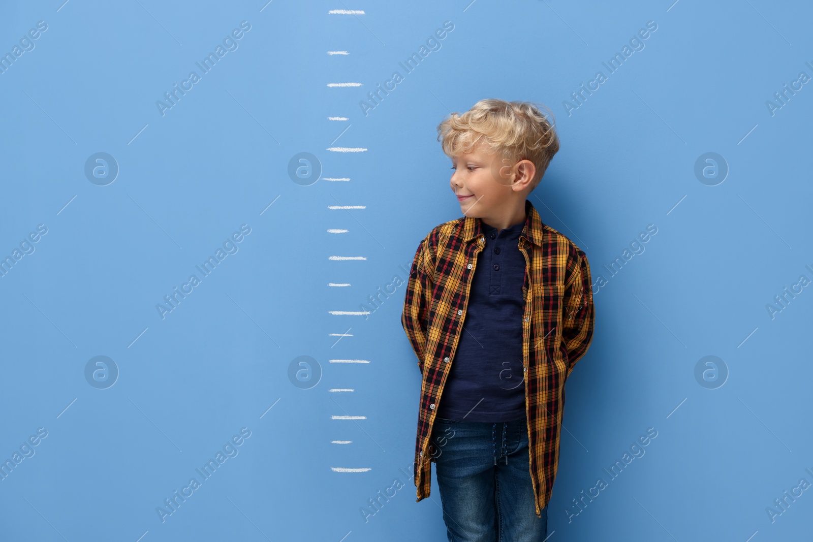 Photo of Cute little boy measuring his height near blue wall