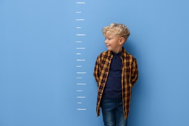 Photo of Cute little boy measuring his height near blue wall