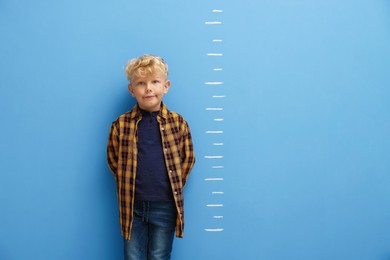 Photo of Cute little boy measuring his height near blue wall