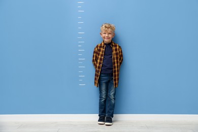 Photo of Cute little boy measuring his height near blue wall