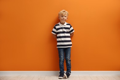 Photo of Cute little boy standing near orange wall