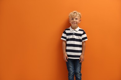 Photo of Cute little boy standing near orange background. Space for text