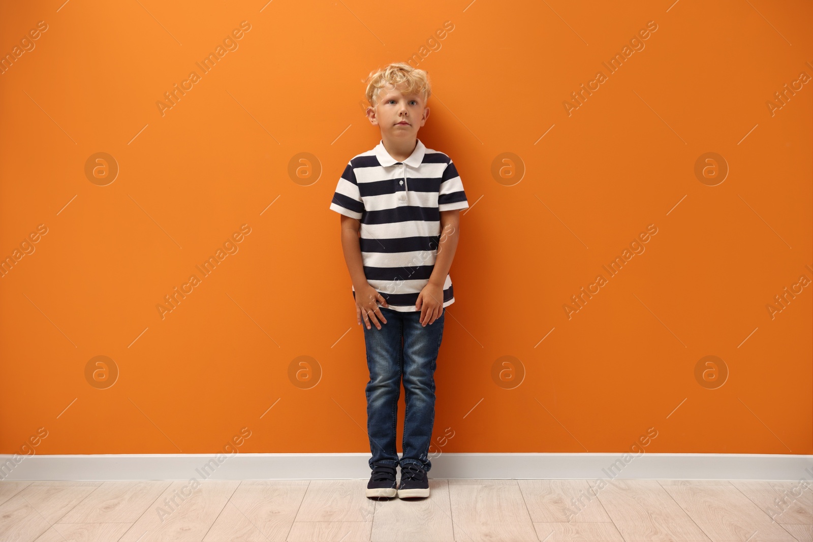 Photo of Cute little boy standing near orange wall