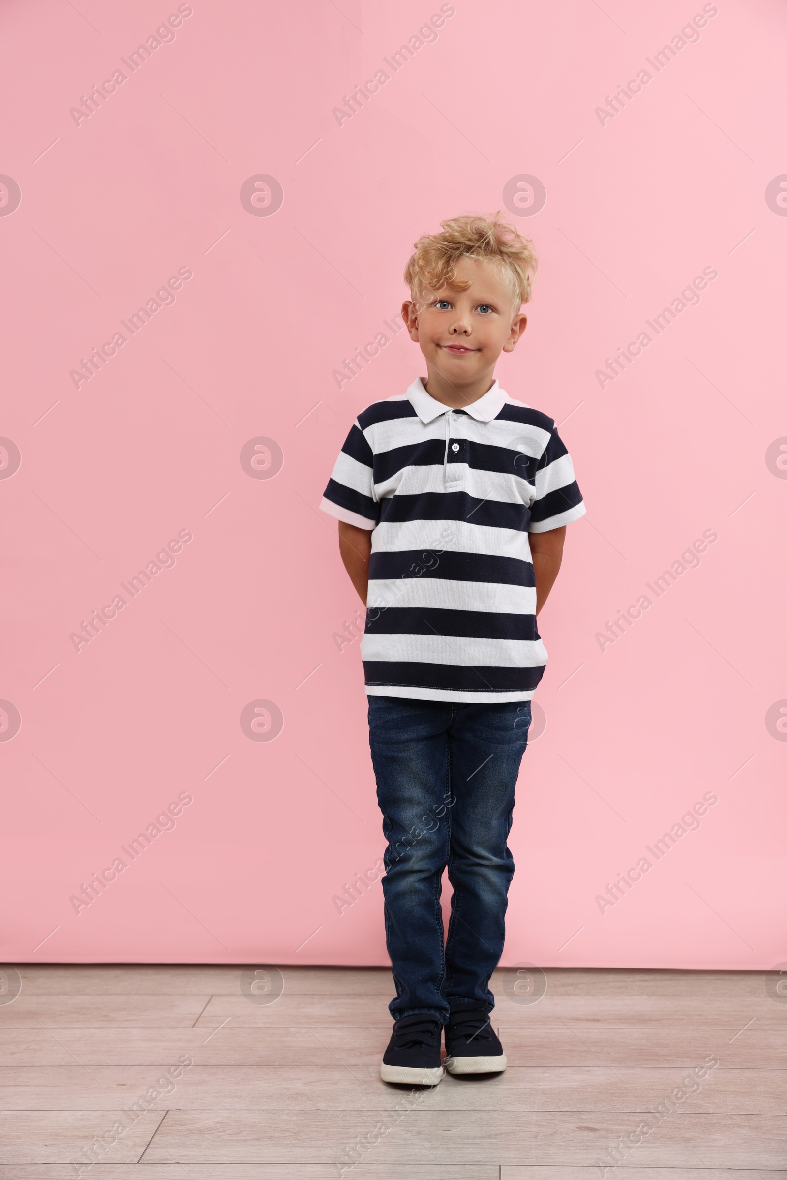 Photo of Cute little boy standing near pink wall