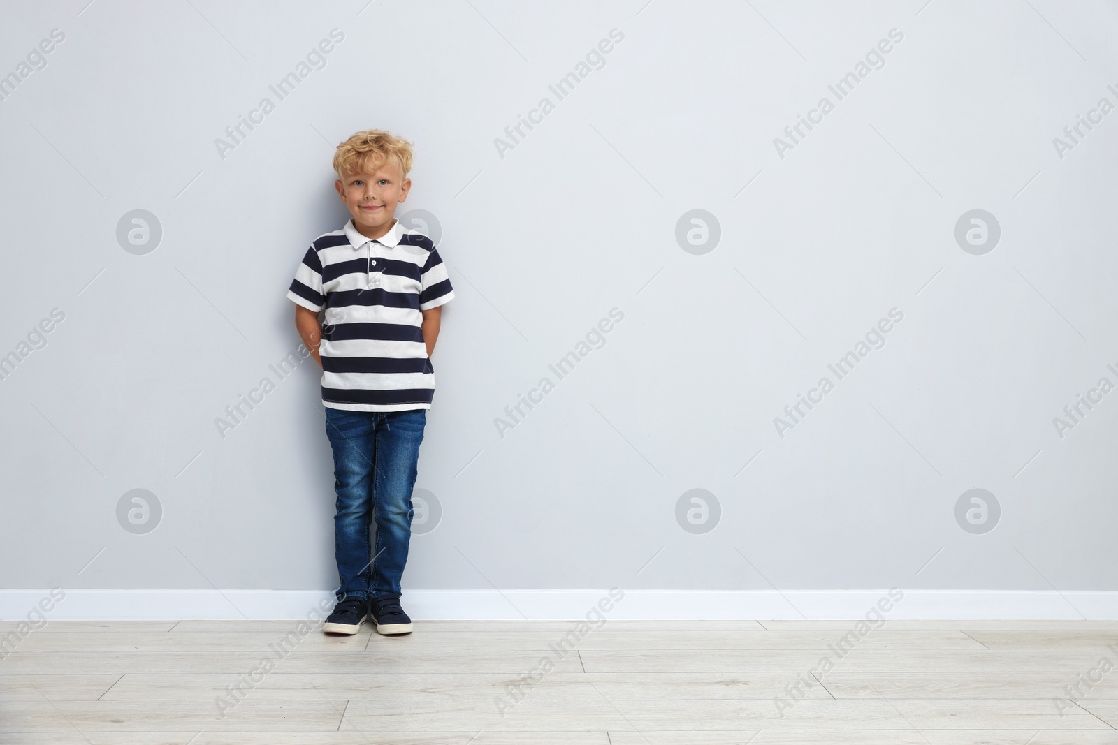 Photo of Cute little boy standing near light wall. Space for text