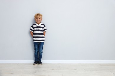 Photo of Cute little boy standing near light wall. Space for text