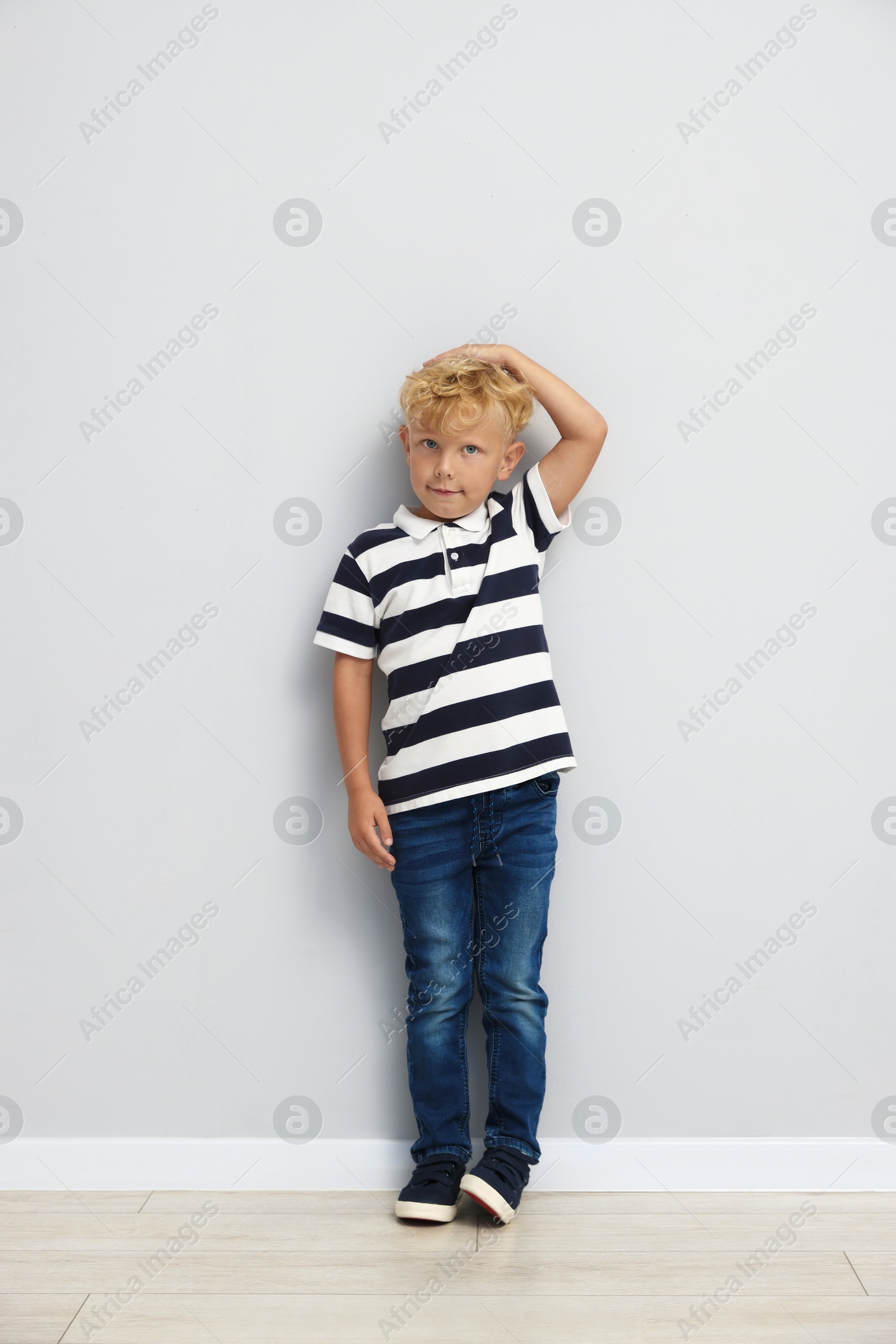 Photo of Cute little boy measuring his height near light wall