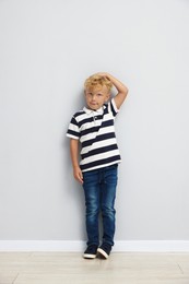 Photo of Cute little boy measuring his height near light wall