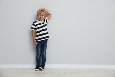 Photo of Cute little boy measuring his height near light wall. Space for text