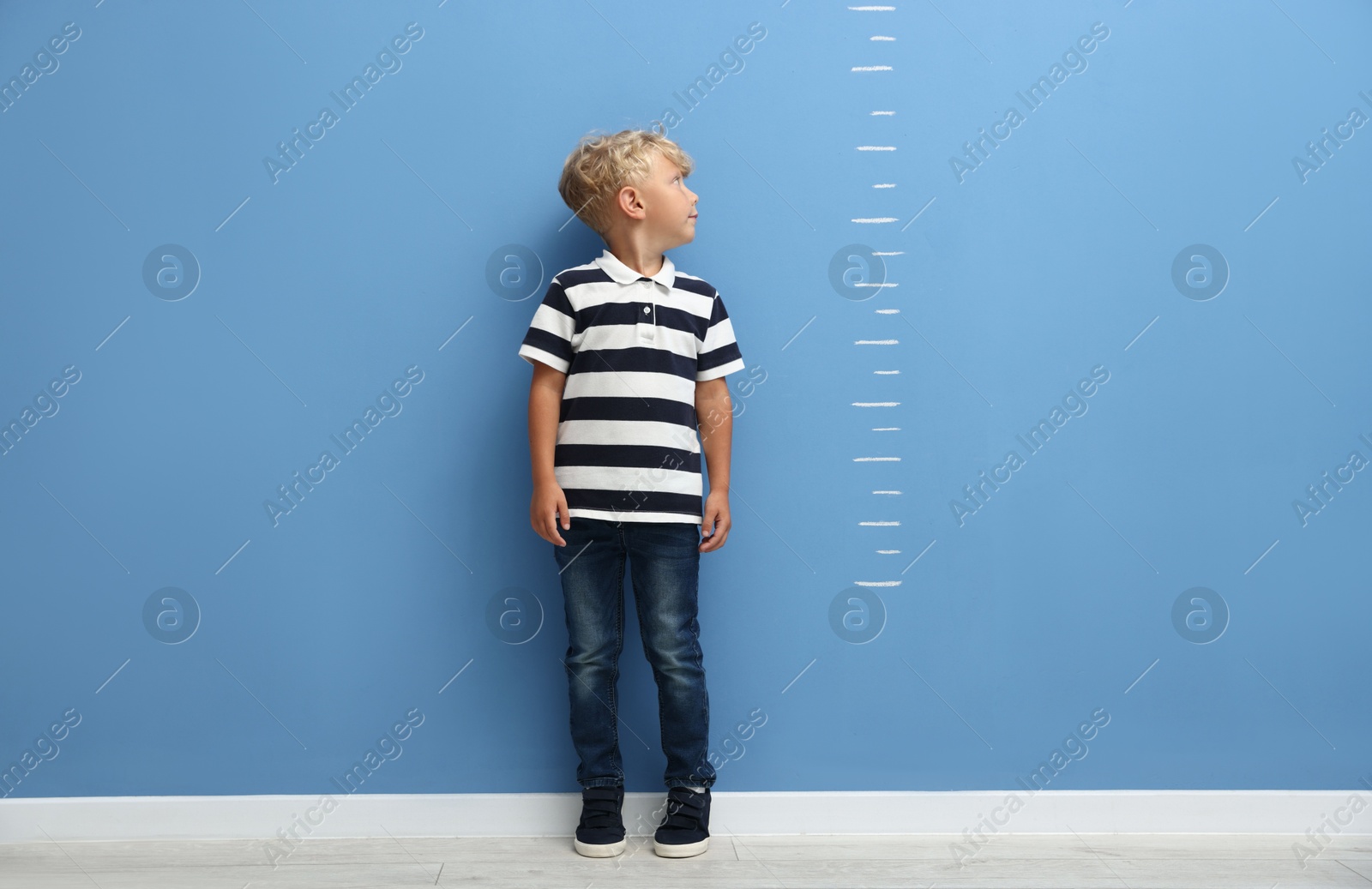 Photo of Cute little boy measuring his height near blue wall