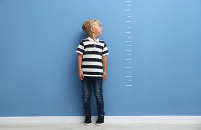 Photo of Cute little boy measuring his height near blue wall