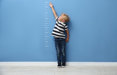 Photo of Cute little boy measuring his height near blue wall