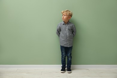 Photo of Cute little boy standing near green wall