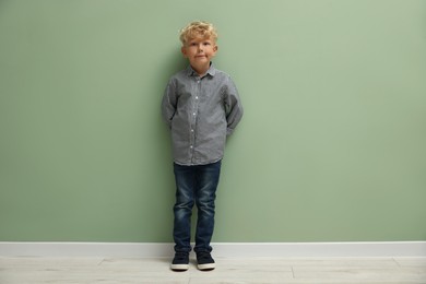 Photo of Cute little boy standing near green wall