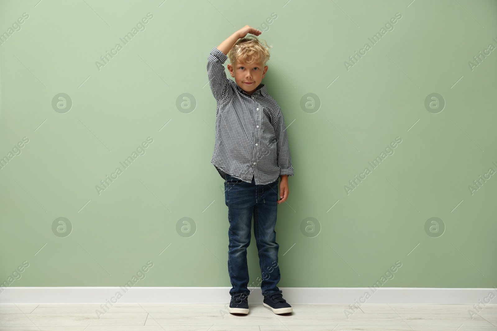 Photo of Cute little boy measuring his height near green wall