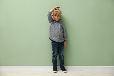 Photo of Cute little boy measuring his height near green wall